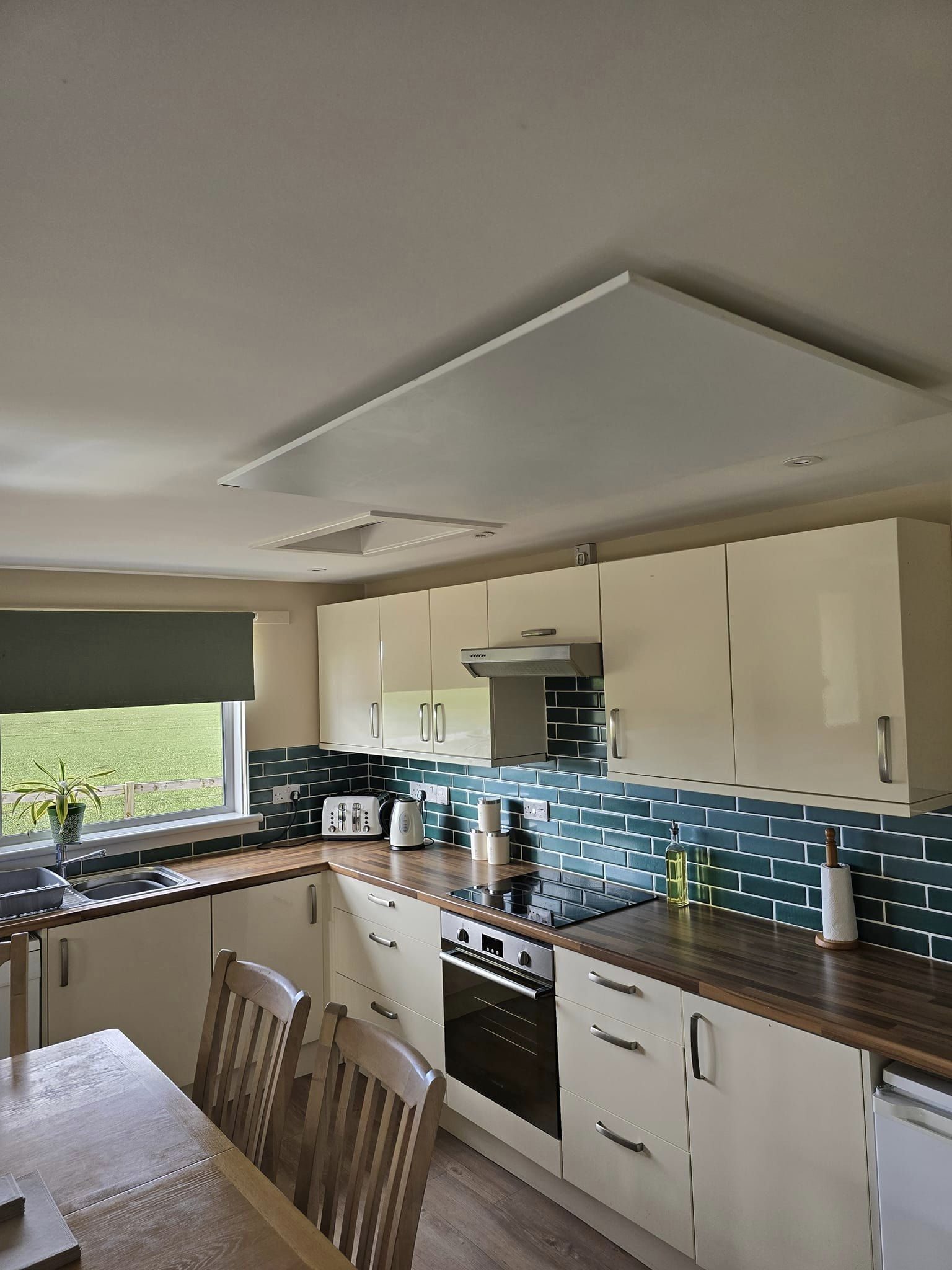 Photo of a white infrared heater installed on the ceiling of the kitchen. The heater is mounted near the centre of the room, with various furniture and decor items visible below.
