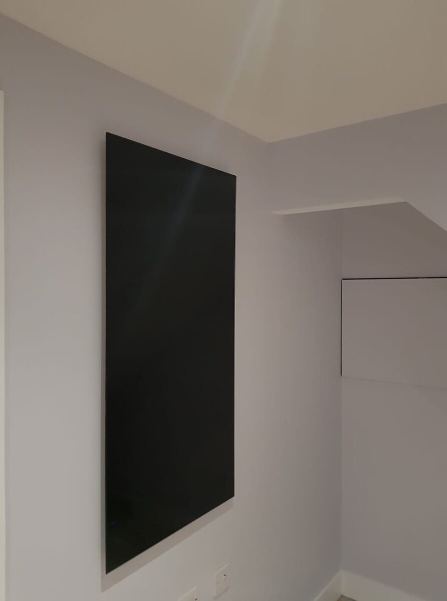 Photo of a large black electric panel heater mounted on a wall. The heater has a sleek, modern design and blends in well with the neutral wall color.